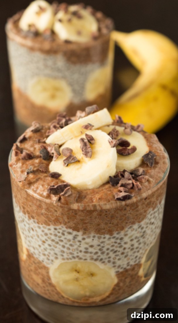 In the foreground, a beautifully layered glass of chocolate and banana chia pudding takes center stage, adorned with fresh banana slices and crunchy cacao nibs. Another glass and a whole banana are softly blurred in the background, creating depth and visual appeal.