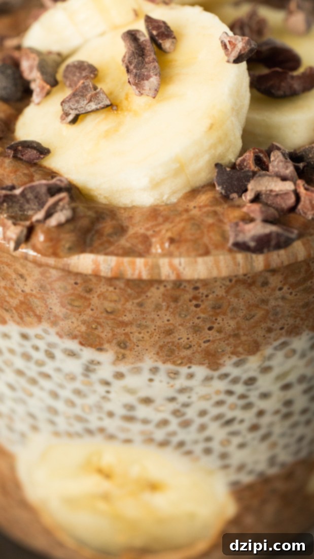 An extreme close-up highlighting the beautiful alternating layers of rich chocolate chia pudding and creamy vanilla chia pudding within a glass. The top is generously garnished with vibrant sliced banana and crunchy cacao nibs, showcasing a perfect texture and visual appeal.
