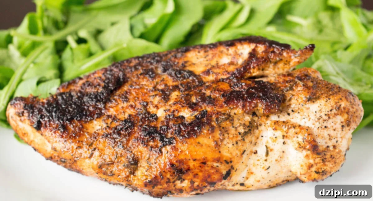 Horizontal view of a plump chicken breast that's been covered in blackening seasoning. A bed of greens sits out of focus in the background.