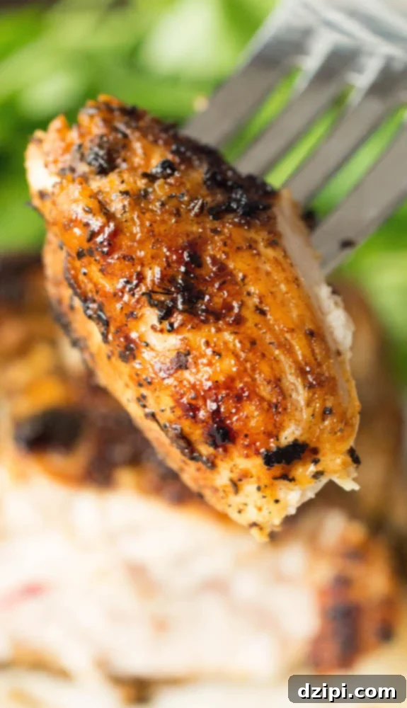 A cut piece of cooked blackened chicken being held up by a fork. The rest of the chicken breast sits out of focus in the background.
