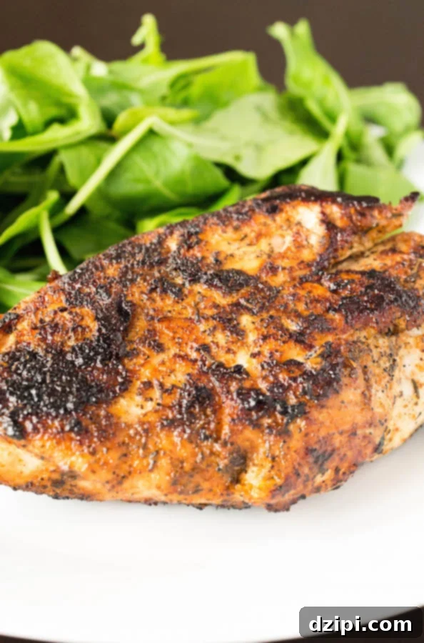 A close up of a blackened chicken breast with a side of spinach on a white plate.
