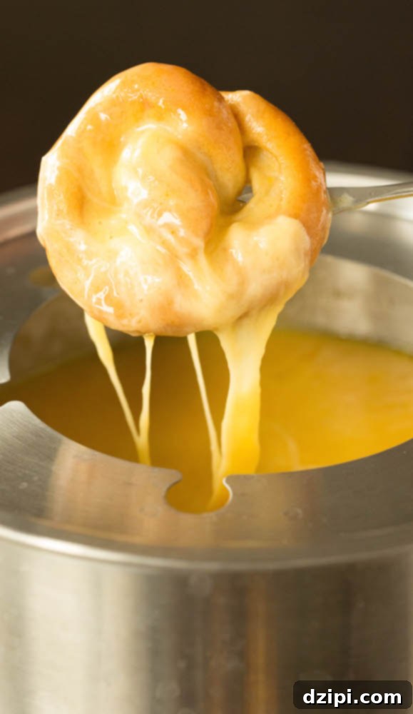 A fondue pot filled with beer cheese has a mini soft pretzel being dipped in.