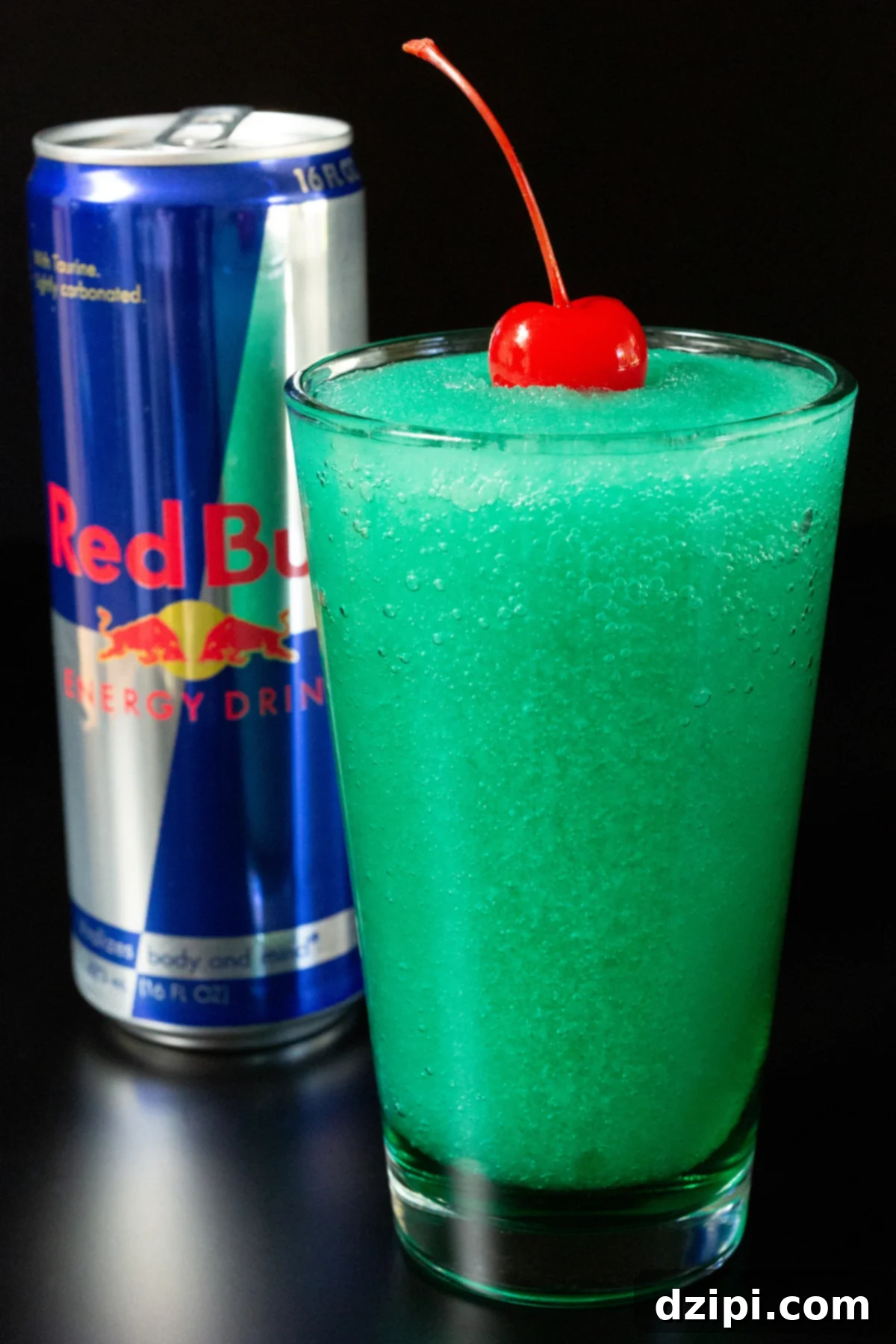 Red Bull Freeze 3 A pint glass is filled with a blue/green slushie that is topped with a maraschino cherry. A can of Red Bull is out of focus in the background.