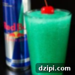 Red Bull Freeze 6 A pint glass is filled with a blue/green slushie that is topped with a maraschino cherry. A can of Red Bull is out of focus in the background.