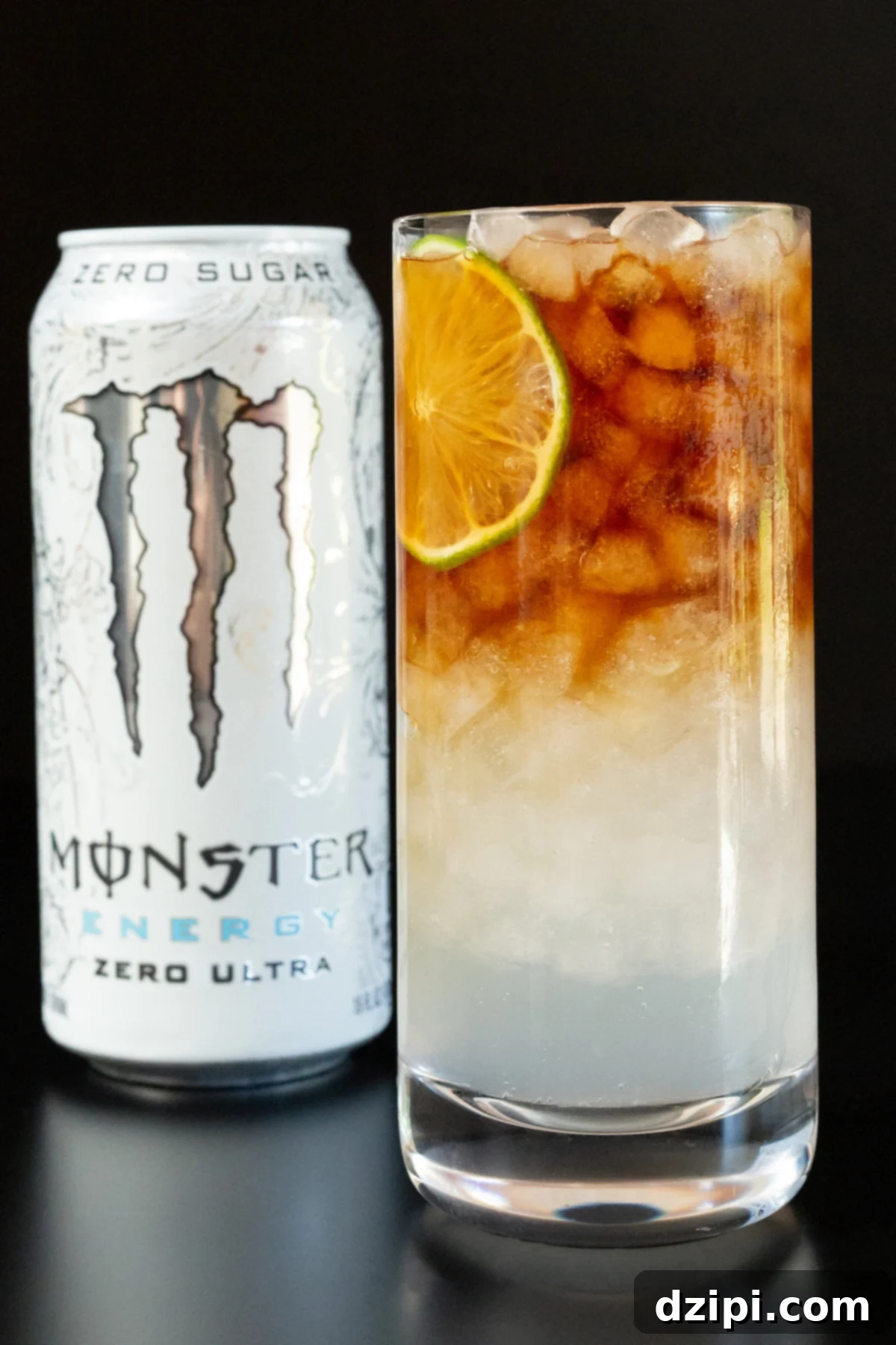 A highball glass filled with layered white Monster Energy drink and dark espresso, garnished with a fresh lime wheel. A can of white Monster is blurred in the background, hinting at the key ingredient.