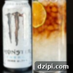 A highball glass filled with layered white Monster Energy and dark espresso, ready to be enjoyed. A can of the energy drink sits out of focus in the background.