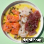 A small white plate with a row of bite-sized raw salmon pieces, raw tuna pieces, and slices of raw scallop surrounded by olive oil and lemon juice. Topped with diced red onion and capers.