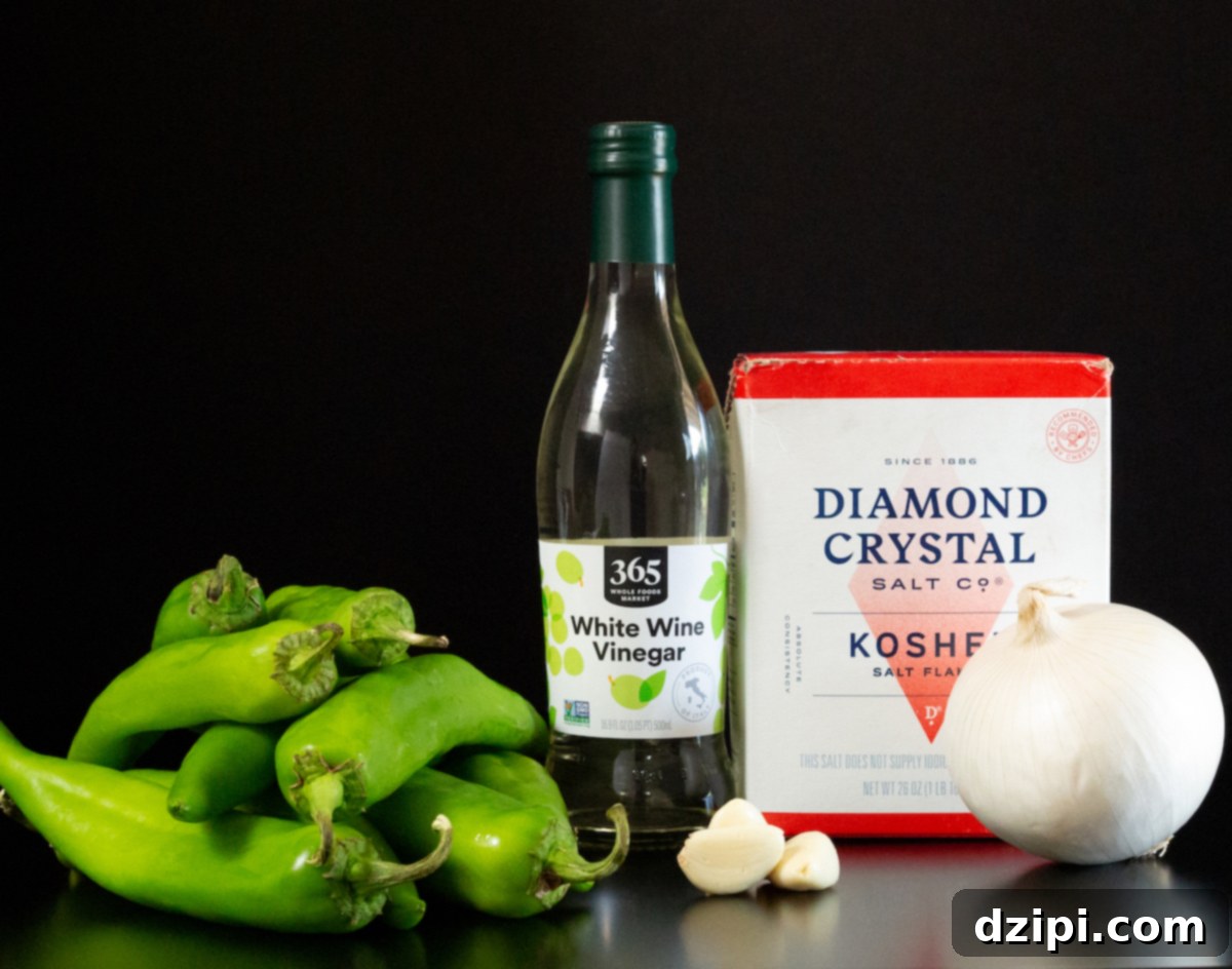 A vibrant display of fresh ingredients for Hatch Chile Hot Sauce: a generous pile of green Hatch chiles, a bottle of crisp white vinegar, a box of Diamond Crystal Kosher salt, three perfectly peeled garlic cloves, and a fresh white onion, all arranged on a sophisticated black background.