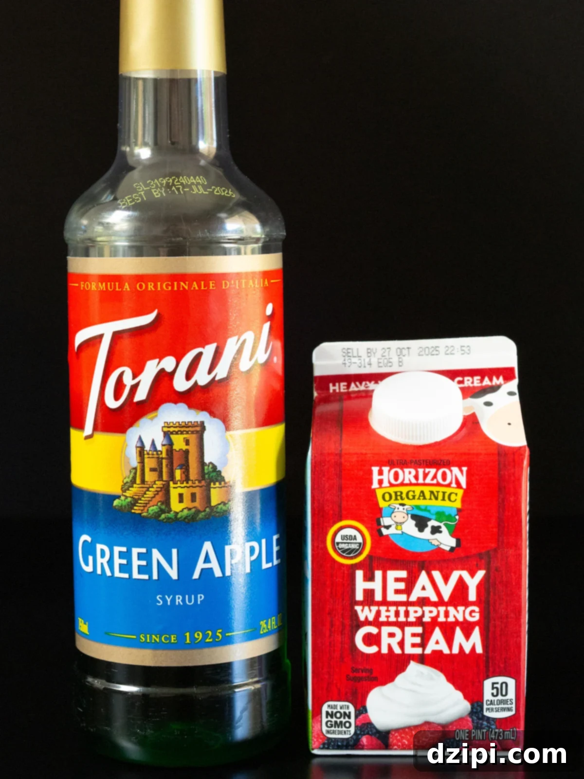 A bottle of Torani brand green apple syrup and a pint of organic heavy cream on a black background.