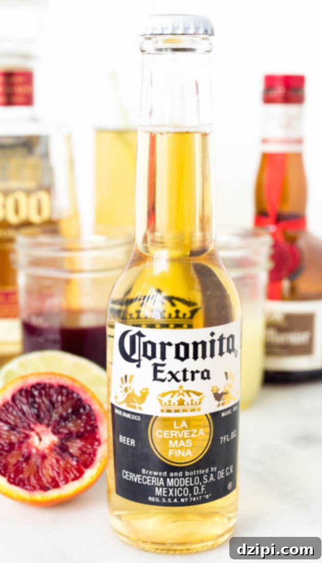 The Perfect Blood Orange Lemongrass CoronaRita 4 A close-up shot of a Blood Orange Lemongrass CoronaRita, showing the inverted Coronita bottle, vibrant orange liquid, ice cubes, and a fresh blood orange slice garnish. The drink rests on a wooden surface with a soft, blurred background.
