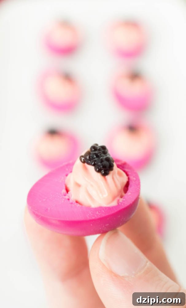 Three fingers delicately hold up a single, miniature pickled deviled quail egg, adorned with a glistening dollop of black caviar. In the blurred background, several more deviled quail eggs are arranged, hinting at a larger spread.