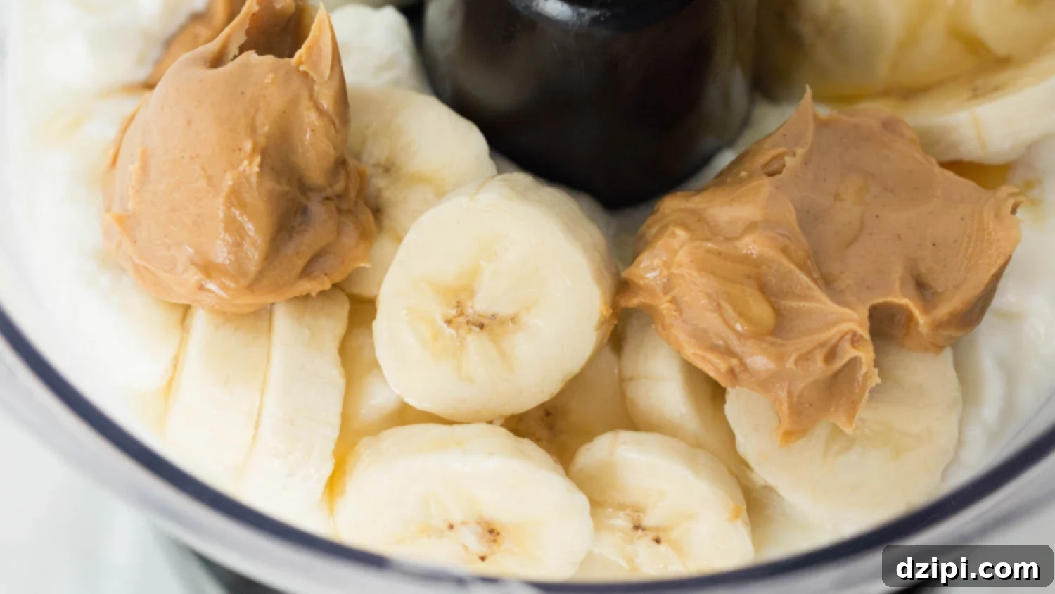 Food processor with yogurt peanut butter banana dog treat ingredients blended into a creamy mixture.