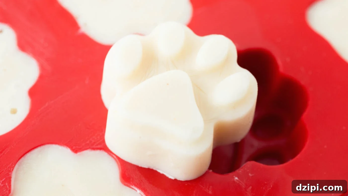 Taking a frozen peanut butter banana dog treat out of the mold, showing its perfect paw shape.