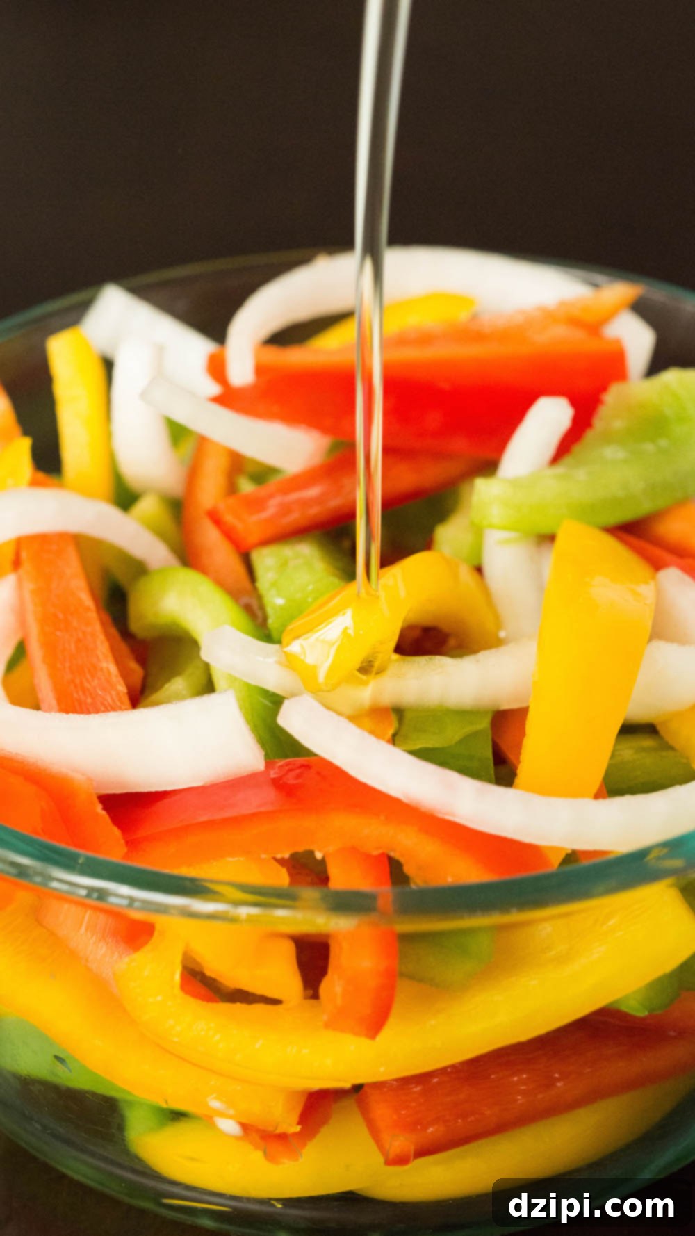 One-Pan Zesty Salmon Fajitas 4 A large glass Pyrex bowl filled with thinly sliced green, red, and yellow bell peppers along with white onions. Olive oil is being drizzled generously over the top, preparing them for seasoning.