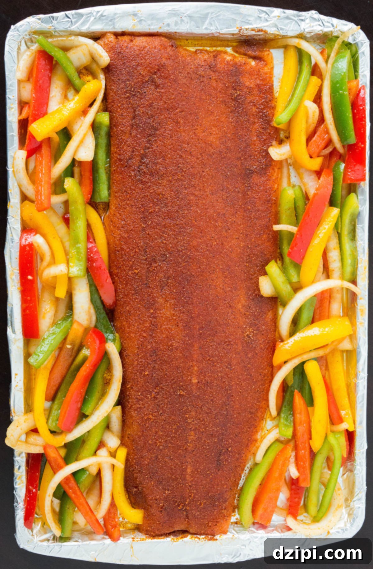 One-Pan Zesty Salmon Fajitas 5 An overhead view captures a generous salmon fillet and an abundance of vibrant, multicolored bell pepper and onion slices artfully arranged on a single sheet pan, ready for roasting.