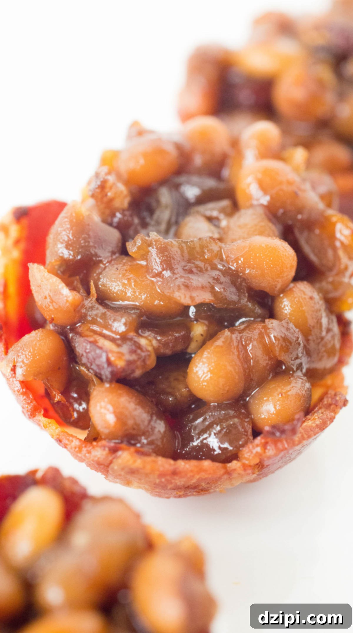 A close-up view of homemade baked beans presented in intricate miniature bacon cups on a rustic wooden surface.