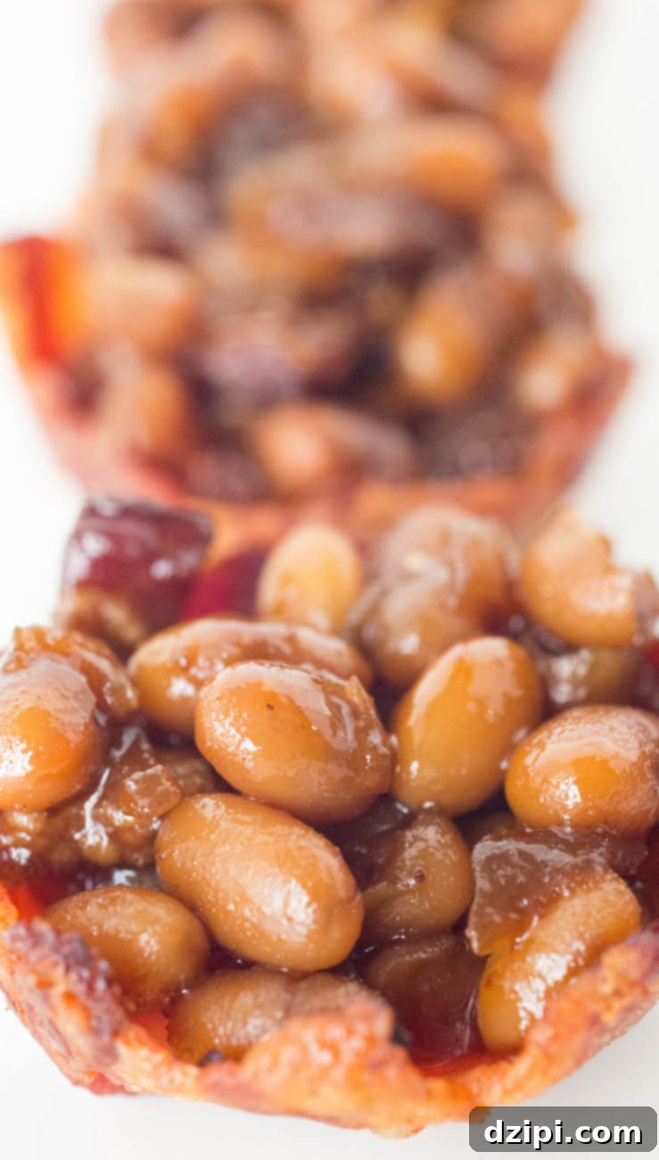 Close-up of freshly prepared homemade baked beans nestled in individual mini bacon cups, garnished and ready to eat.