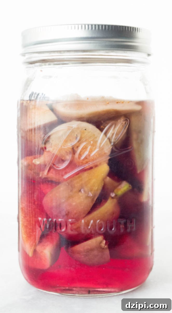 Homemade Fig Vodka Elixir 5 A charming jar of beautifully tinted pink homemade fig infused vodka rests on a pristine white background, exuding elegance and inviting sips.