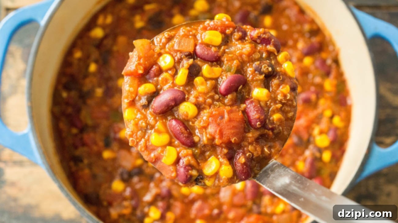 Overhead a dutch oven that's filled with meatless chili. A metal ladle holds up a scoop of it so you can see the individual beans, tomato, corn, and quinoa.