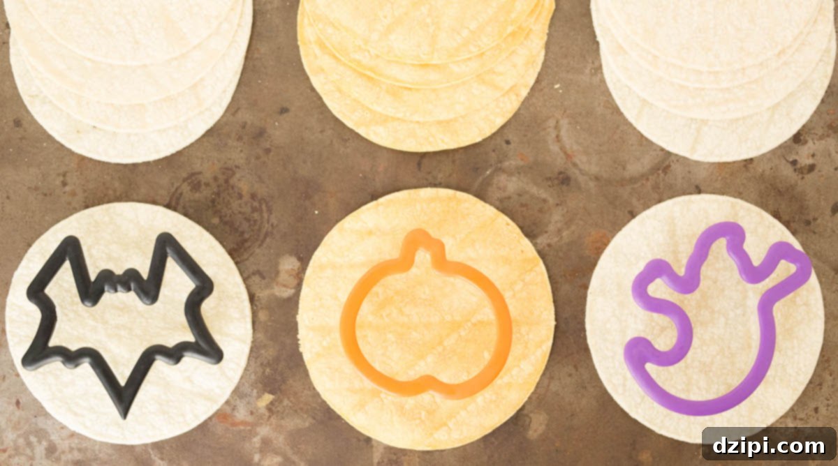 Spooktacular Tortilla Chip Trio 3 Three Halloween-themed cookie cutters – a ghost, a pumpkin, and a bat – are actively cutting shapes from various corn tortillas laid out on a clean cutting board, illustrating the creative and easy first step of making homemade festive chips.