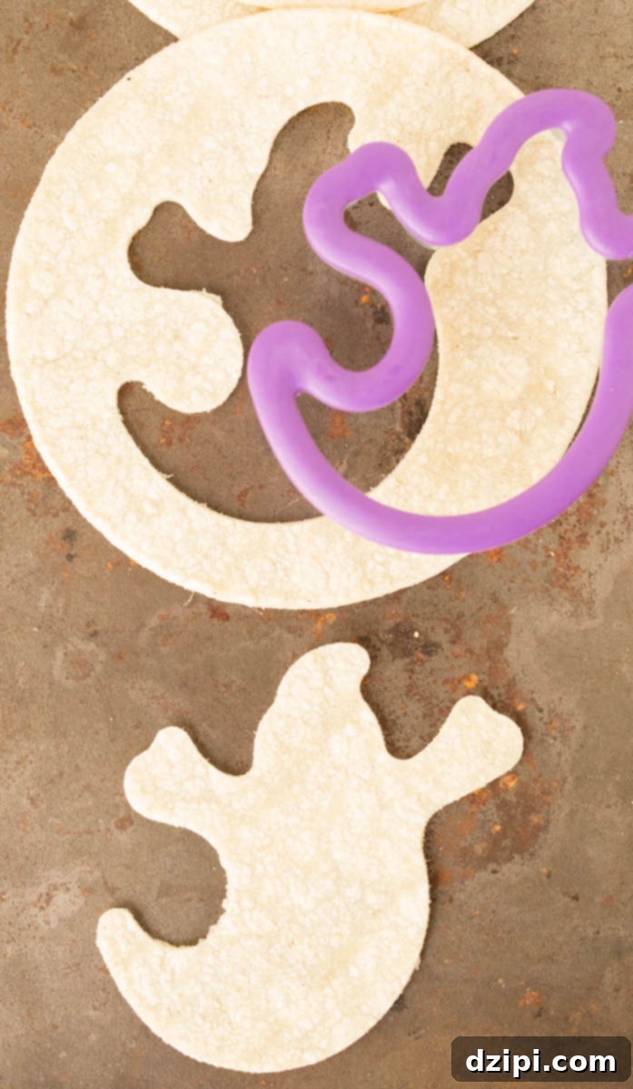Spooktacular Tortilla Chip Trio 4 A Halloween ghost cookie cutter is precisely pressing into a light-colored corn tortilla, illustrating the initial and fun step of shaping the festive chips before seasoning and baking.