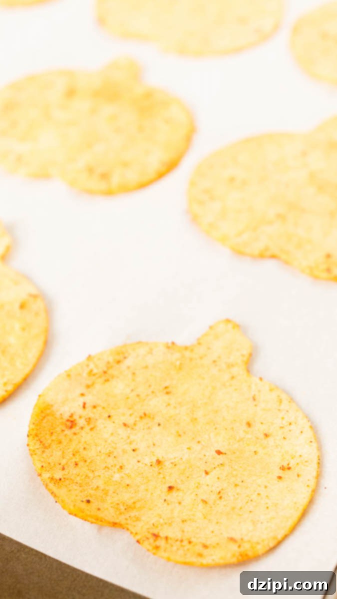 Spooktacular Tortilla Chip Trio 6 A baking sheet holds an array of freshly baked, golden-brown pumpkin-shaped Halloween tortilla chips, expertly seasoned with a spicy blend, cooling on parchment paper and ready to be served as a delightful festive snack.