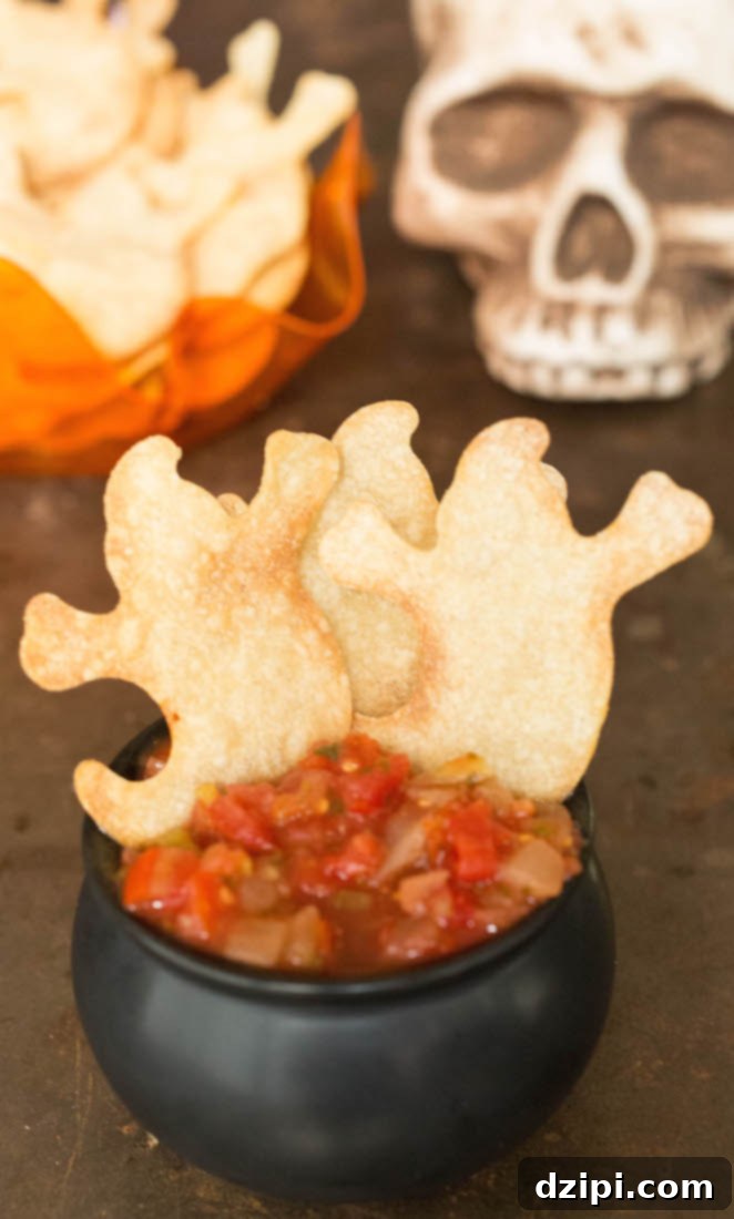 Spooktacular Tortilla Chip Trio 7 Crispy ghost-shaped tortilla chips, seasoned with a refreshing hint of lime and coarse salt, are served alongside a whimsical black cauldron brimming with vibrant red salsa, creating a perfectly spooky and incredibly delicious Halloween snack display.