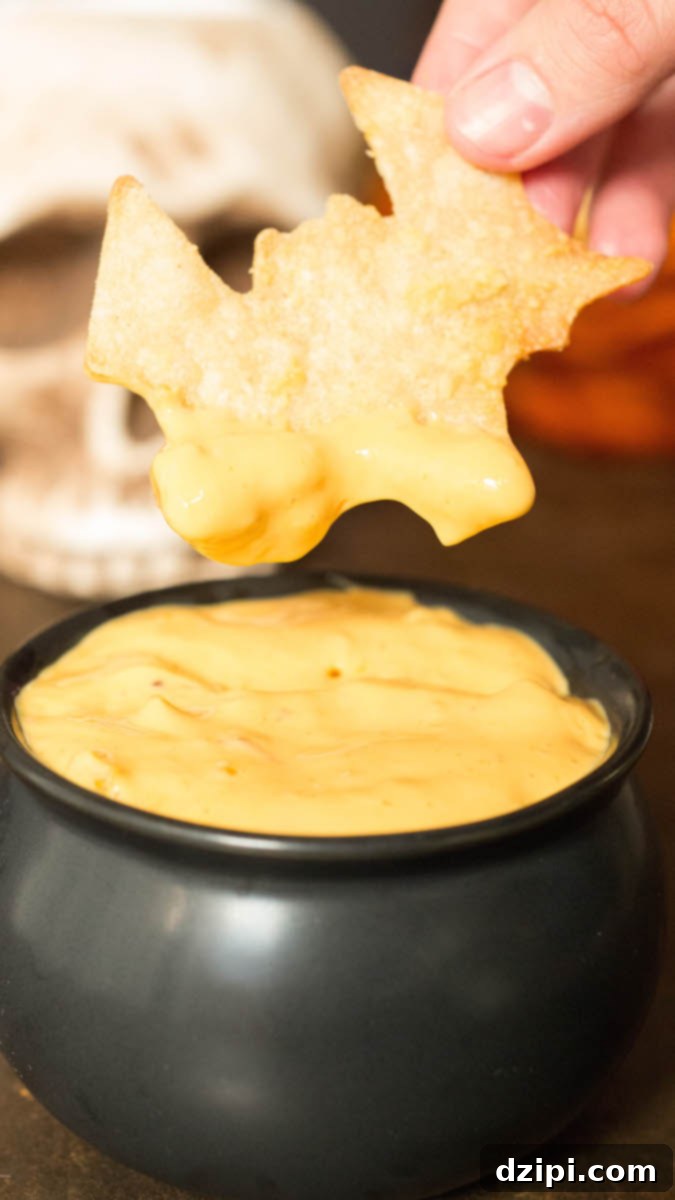 Spooktacular Tortilla Chip Trio 9 Crispy garlic parmesan bat-shaped tortilla chips are captured mid-dip, plunging into a whimsical black cauldron filled with gooey, golden melted queso, presenting a savory and playfully spooky Halloween snack idea.