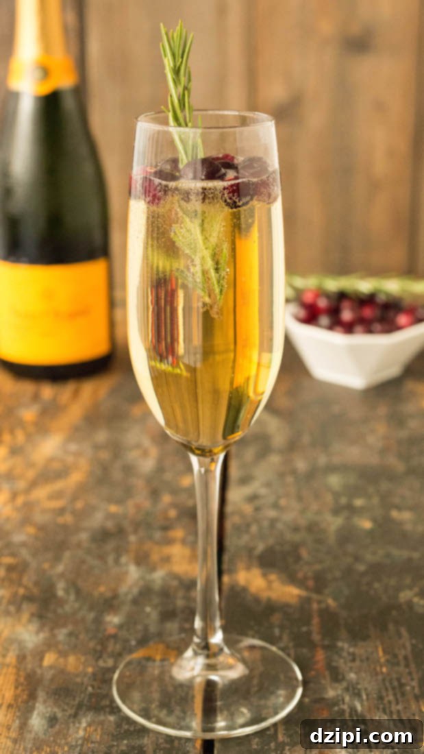 A White Grape Cranberry Mimosas in a champagne flute with rosemary sprig.
