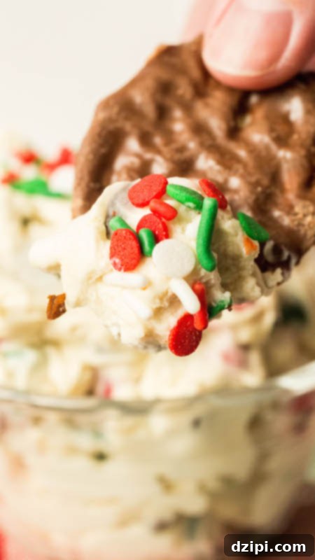 A crisp chocolate potato chip is gracefully dipped into a rich and festive Christmas Cookie Dough Dip, showcasing its delightful texture and sprinkles.