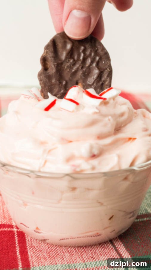 A hand gently dips a Dark Chocolate Wavy Lay's potato chip into a light and fluffy Peppermint Fluff Christmas Dip, showing the perfect texture for scooping.
