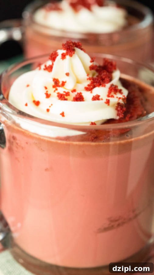 Crimson Velvet Cocoa 3 Close up of a Red Velvet Hot Chocolate, featuring a piece of cake submerged in the drink, topped with a generous swirl of Cream Cheese Whipped Cream and cake crumbs.