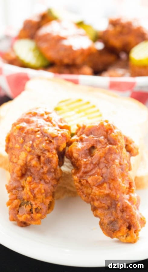 Two glistening Nashville Hot Fried Chicken Wings presented with a slice of white bread and a pickle, showcasing traditional serving style.