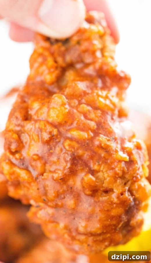 A Nashville Hot Fried chicken wing with rich, red spicy sauce dripping, emphasizing its intense flavor and juicy texture.