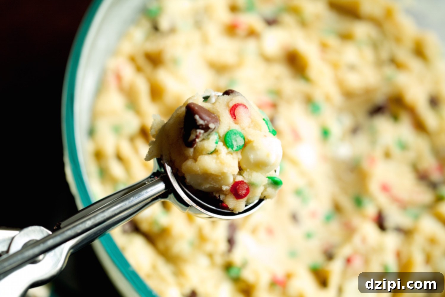 Holiday Cake Batter Cookie Bliss 2 Christmas cookie batter being scooped up in a small round metal cookie scoop, showing red and green sprinkles within the dough.