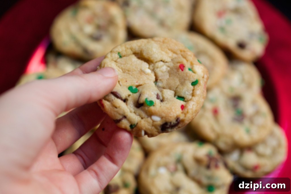 Holiday Cake Batter Cookie Bliss 4 A hand holding a freshly baked Christmas cake batter cookie, showcasing its soft texture and colorful red and green circle sprinkles.