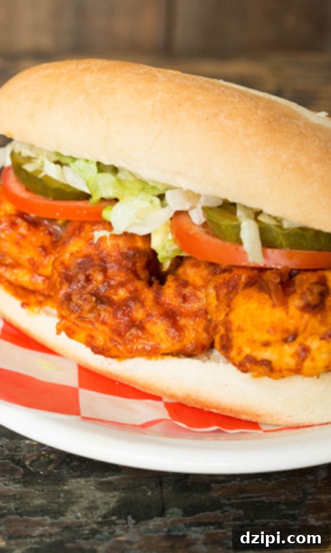 A homemade Nashville Hot Shrimp Po' Boy, artfully arranged with crisp shredded lettuce, ripe tomato slices, and tangy dill pickles, ready to be devoured.