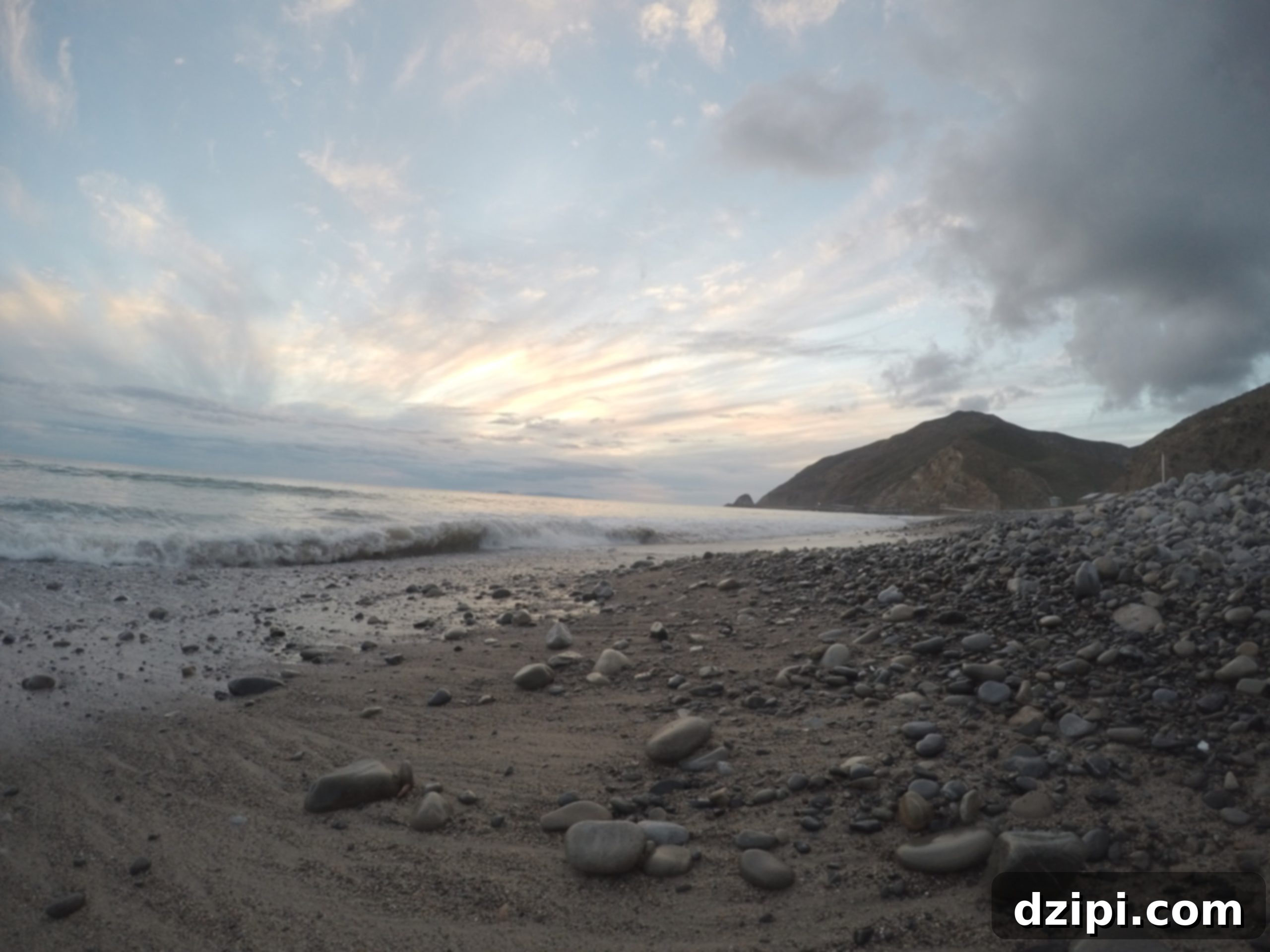 Stunning view of Point Mugu Campground with the ocean, mountains, and a rugged coastline at sunset.
