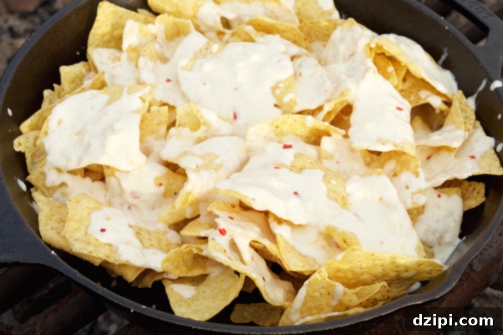 Close-up of creamy garlic sauce generously drizzled over a layer of tortilla chips for pizza nachos.