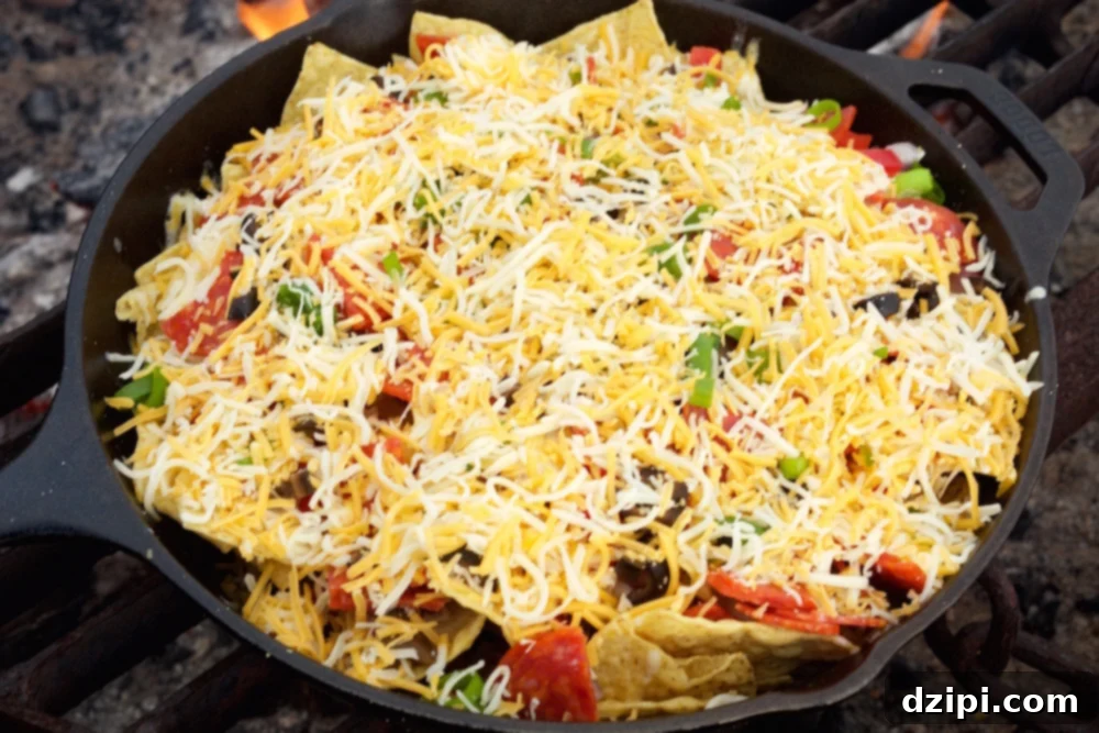 Uncooked Campfire Pizza Nachos in a cast iron skillet, topped with shredded cheese, pepperoni, and vegetables, ready for melting.