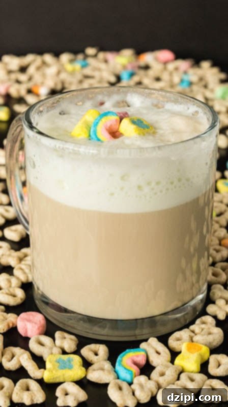 Close-up of a frothy Lucky Charms Cereal Milk Latte in a clear mug, garnished with bright marshmallows, with loose cereal scattered around for aesthetic.