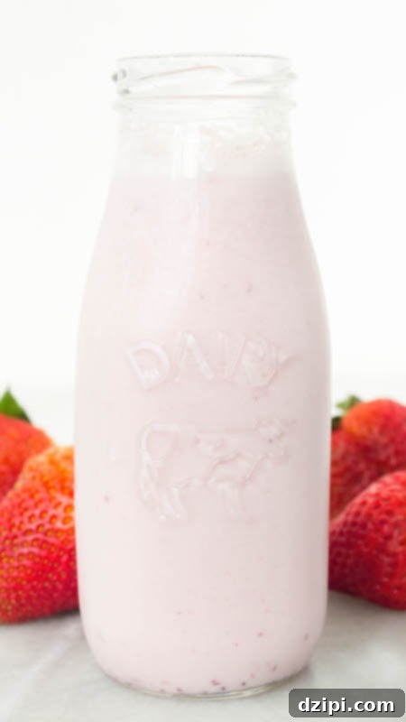 Homemade Strawberry Milk Recipe in a glass milk bottle next to fresh strawberries.