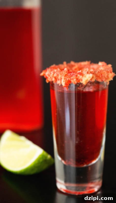 A glass of homemade Flamin' Hot Cheetos infused vodka, glowing with a reddish hue, with a lime slice elegantly placed in the soft-focus background.