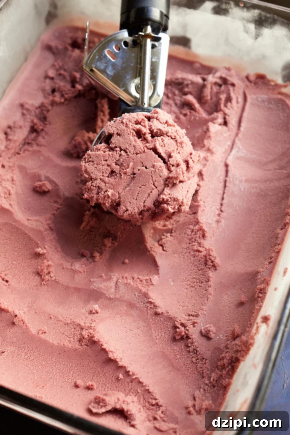 Scooping rich, homemade red wine ice cream into a glass, highlighting its smooth texture.