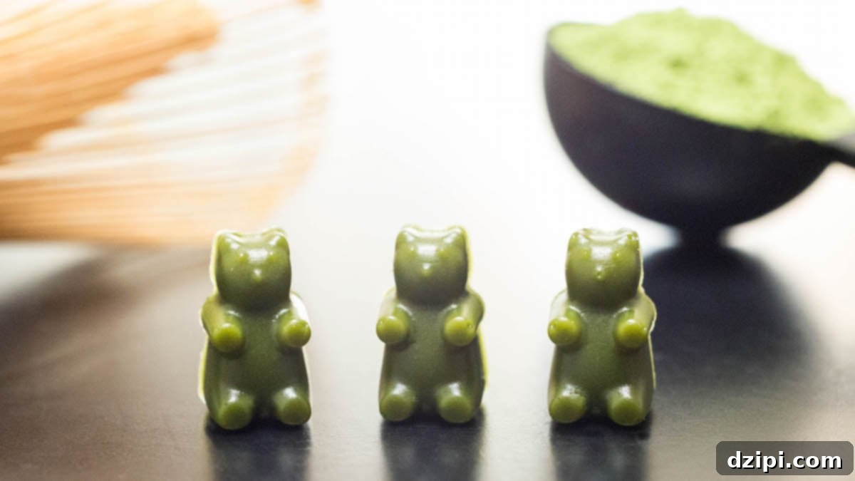 Three homemade vibrant green matcha gummy bears, a bamboo whisk, and scattered matcha powder on a surface, highlighting the ingredients and delicious result.