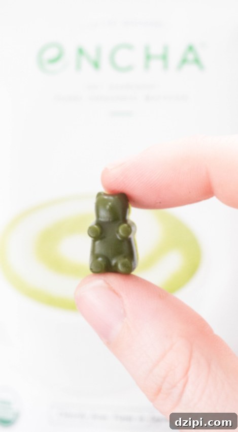 Close-up of a hand holding a single vibrant green matcha gummy bear, showcasing its appealing texture and perfect shape.