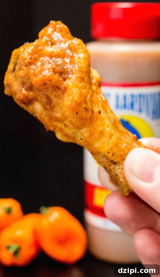 A hand reaching for a perfectly sauced Secret Aardvark Chicken Wing, highlighting its crispy texture and vibrant color.