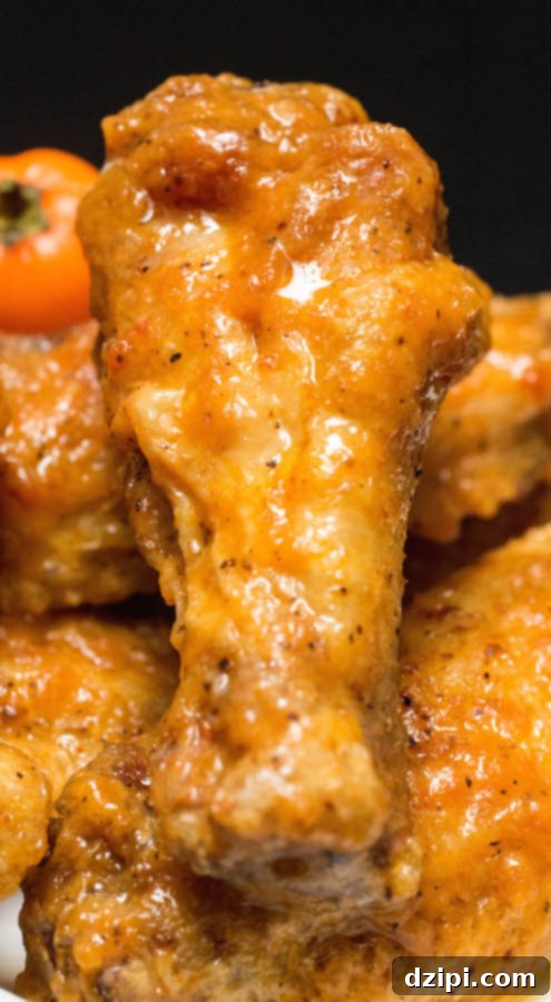 A close-up of a Secret Aardvark Chicken Wing, showcasing the rich, reddish-orange sauce coating and perfectly cooked skin.