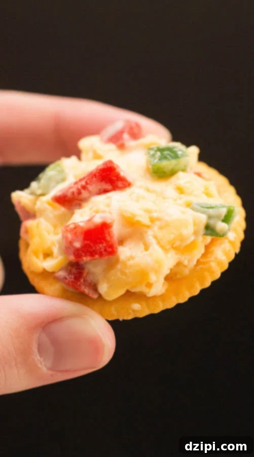 Fingers holding a Ritz cracker with Pimento Cheese, ready to be enjoyed.