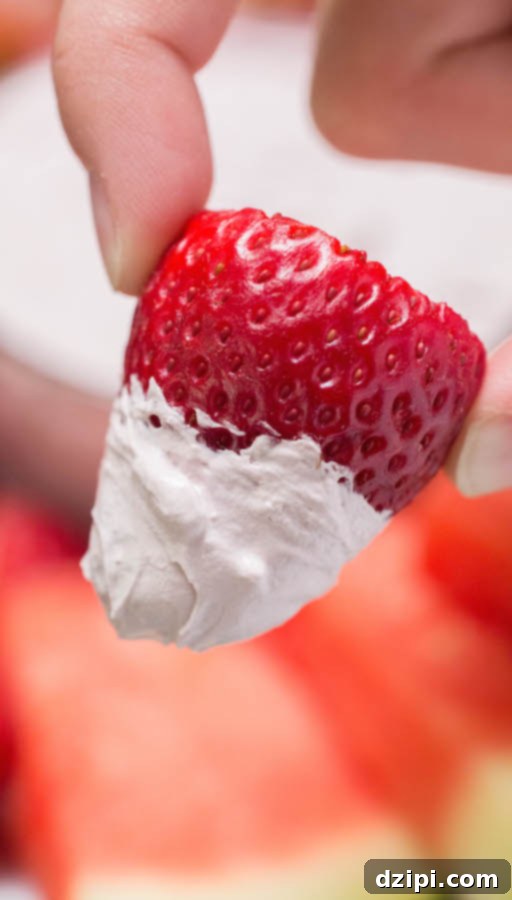 A hand holds up a fresh strawberry that's been generously dipped in the velvety Red Wine Fruit Dip.